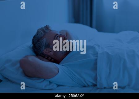 Schlafloser Mann mittleren Alters, der nachts im Bett liegt Stockfoto
