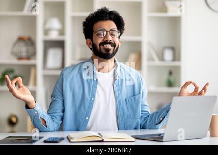 Zen-Konzept. Lächelnder Indischer Mann Meditiert Am Arbeitsplatz Im Home Office Stockfoto