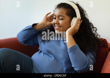 Fröhliche junge hispanische Frau in Übergröße, die Musik hört Stockfoto