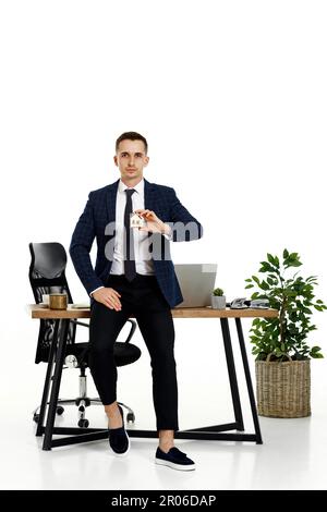 Erfolgreicher weißer Geschäftsmann, der ein Spielzeughaus im Büro hält. Immobilienversicherung Stockfoto