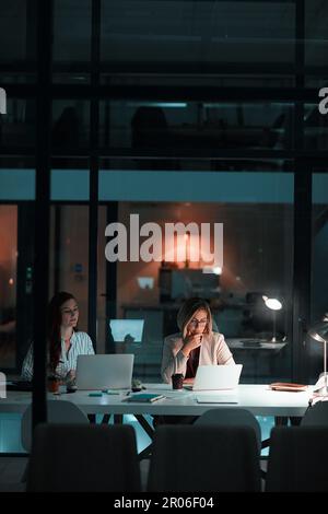 Der Beweis liegt in der Hingabe. Zwei Kollegen, die ihre Laptops in einer späten Nacht in einem modernen Büro verwenden. Stockfoto