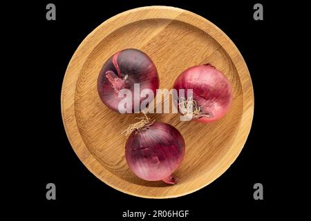 Drei organische blaue Zwiebeln in einer Holzschale auf schwarzem Hintergrund, Makro, Draufsicht. Stockfoto