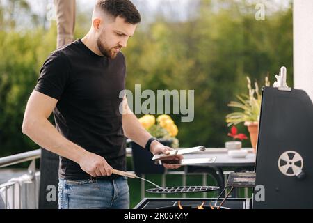 Seitenansicht eines gutaussehenden Mannes, der ein Lagerfeuer vorbereitet, um Steak im Grill zu machen Stockfoto