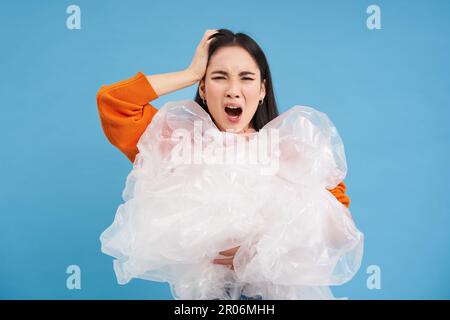 Umweltaktivismus und Recycling. Junge asiatische Frau mit lästigem Gesicht, müde von Unwissenheit für die Umwelt, hält Plastikabfall in der Hand, sieht verärgert aus Stockfoto