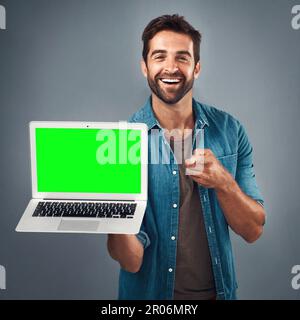 Ich habe das gesehen und an dich gedacht. Studiofoto eines gutaussehenden jungen Mannes, der ein Notebook mit grünem Bildschirm vor grauem Hintergrund zeigt. Stockfoto