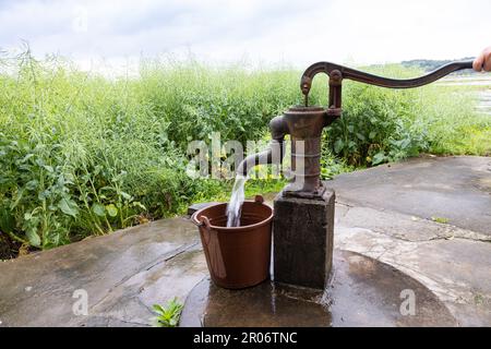 Menschen, die den Eimer mit Wasser aus der Handpumpe füllen, graben von Hand in flachen Grundwasserleitern in Dörfern auf dem Land in China. Rapssamen-Hülsen, Stiele, o Stockfoto