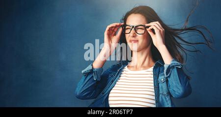 Absolut umwerfend. Studiofoto einer jungen Frau, die vor blauem Hintergrund Luft ins Gesicht geblasen hat. Stockfoto