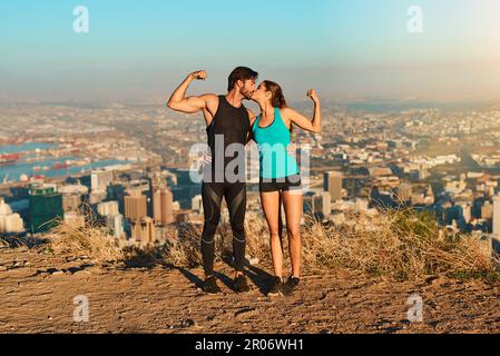 Werden Sie zum Power-Pärchen beim Workout. Aufnahme über die gesamte Länge eines jungen Paares, das sich während des Trainings in die Muskeln bewegt und sich küsst. Stockfoto