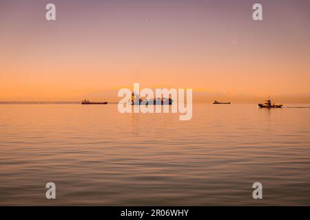 Große Frachtschiffe, die bei Sonnenuntergang in Thessaloniki, Griechenland, auf einer riesigen Ausdehnung des offenen Wassers segeln Stockfoto