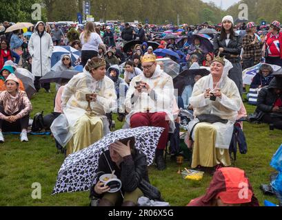 Drei Personen, die falsche Kronen und Regenmäntel tragen, rauchen Zigaretten und trinken aus Bechern im Hyde Park, London, Großbritannien. Im stetigen Regen, ein Meer von patriotischen Br Stockfoto