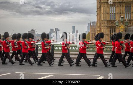 Mit ihren Gewehren marschieren Soldaten der Grenadiergarde der britischen Armee in voller Zeremonialkostüm über die Westminster Bridge und vorbei an den Häusern Stockfoto