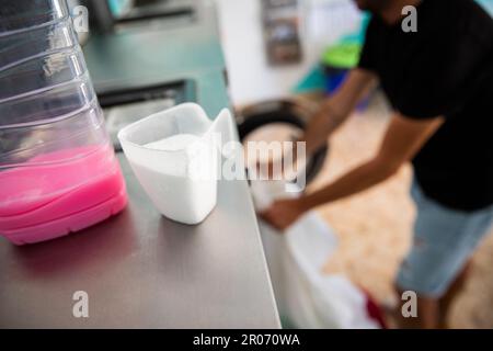 Ein Mann lädt die Waschmaschine in einen Waschsalon, Nahaufnahme des Waschmittels und Weichmachers Stockfoto