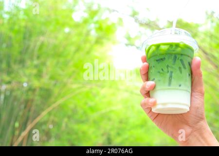 Eine Frau, die den Glas-Ice Matcha Latte grünen Tee-Kaffee im Frühling Natur-Hintergrund hält Stockfoto