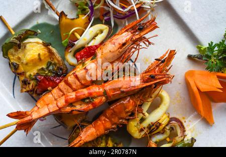 Gegrillte Garnelen mit Fisch auf Spießen auf isoliertem schwarzem Hintergrund, Draufsicht Stockfoto