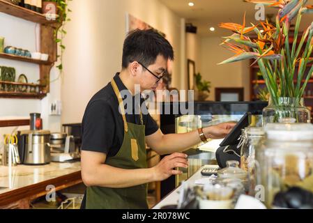 Vietnamesischer Kellner, der an der Theke arbeitet, mit einem Automaten in einem Café Stockfoto