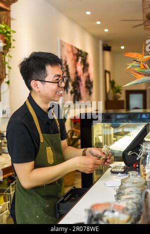 Vietnamesischer Kellner, der an der Theke arbeitet, mit einem Automaten in einem Café Stockfoto