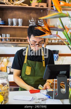 Vietnamesischer Kellner, der an der Theke arbeitet, mit einem Automaten in einem Café Stockfoto