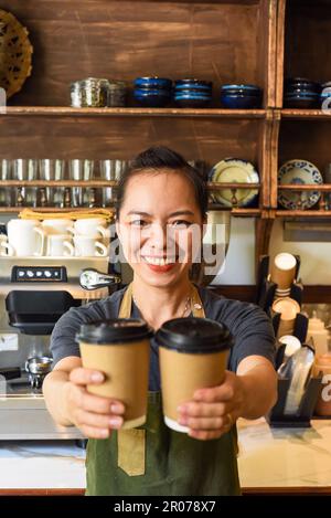 Vietnamesische lächelnde Kellnerin hielt Pappbecher mit Kaffee in einem Café Stockfoto