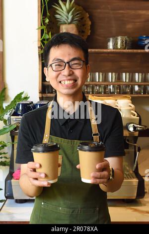 Vietnamesischer lächelnder Kellner hielt Pappbecher mit Kaffee in einem Café Stockfoto