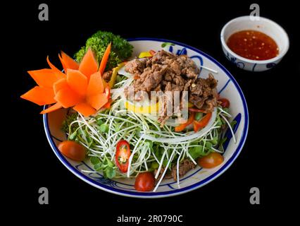 Vietnamesisches gebratenes Rindfleisch mit Salat und Sauce auf schwarzem Hintergrund für ein Menü Stockfoto