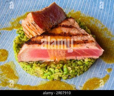 Thunfischsteak Medium, selten serviert mit Erbsen, isoliert auf schwarzem Hintergrund, Seitenansicht Stockfoto