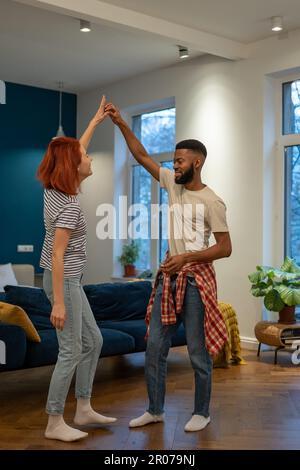 Liebevolles junges, vielfältiges Paar, das romantischen Tanz im modernen Schlafzimmer mit Panoramafenstern tanzt. Stockfoto