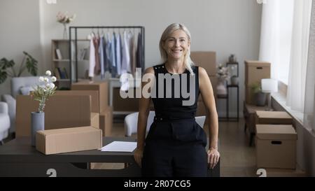 Erfolgreicher, zufriedener Besitzer eines kleinen Internet-Shops, der am Arbeitsplatz posiert Stockfoto