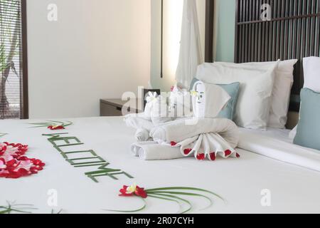 Begrüßungsgetränke mit Blumen und Handtüchern auf dem Bett im Luxushotel bei der Ankunft. Stockfoto