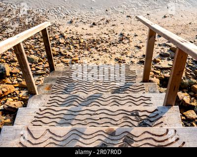 Weg zum Strand. Leere Holztreppen am Sandstrand, Felsen und Meerwasser Hintergrund. Sommerurlaub und Urlaubsreisekonzept. Stockfoto