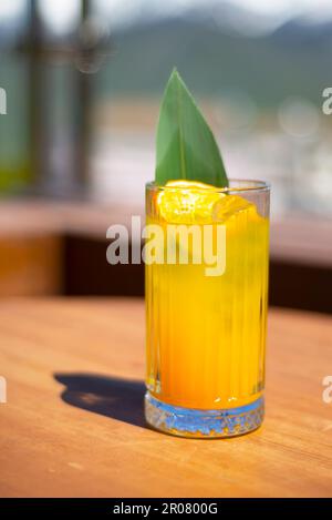 Ein Glas mit einem Cocktail, Saft, Limonade auf einem Tisch in den Bergen. Ruh Dich Aus. Entspann Dich. Fruchtiges Getränk mit grünen Blättern und orangefarbenen Chips. Stockfoto