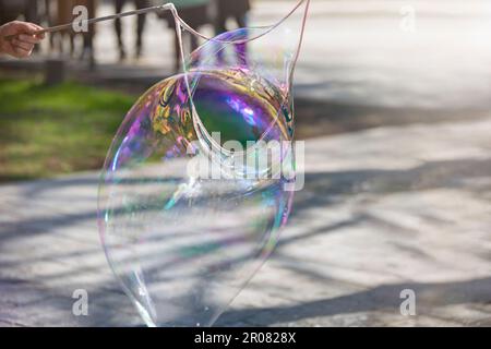 Ein Mann macht eine riesige Seifenblase im Park. Sommerspaß im Park für die ganze Familie. Stockfoto