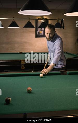 Stilvoller, weiß-bärtiger Mann, der Billard spielt. Steht neben dem Tisch. Stockfoto