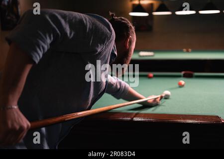 Ein Mann versucht, den Ball mit Blick auf den Billard von hinten zu treffen. Billardzimmer im Hintergrund. Stockfoto