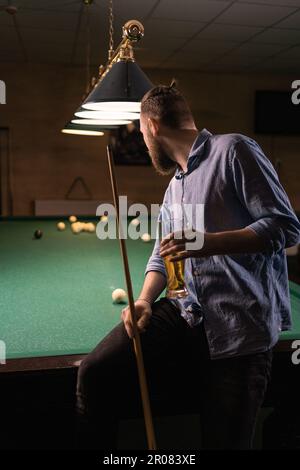 Ein Millennialmann, der Spaß an einem Abend im Billardclub hat und Bier trinkt Stockfoto