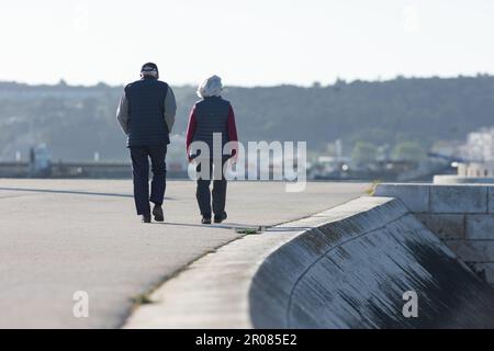 Ein älteres Paar geht am Ufer entlang in der Nähe eines Betonabhangs Stockfoto