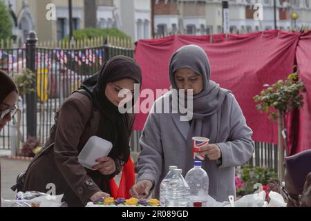 Croydon, Greater London, Großbritannien. 7. Mai 2023. Die Krönungsfeier von König Charles III. Geht weiter mit vielfältigen Mittagessen, Partys und Versammlungen im ganzen Land - hier in der Baitus Subhan Moschee in Croydon. Einheimische Frauen trinken auf die königliche Krönung aus einem Union Jack Cup Credit: Motofoto/Alamy Live News Stockfoto