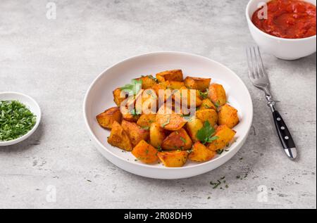 Traditionelle spanische Kartoffel, Patatas bravas mit geräucherter Paprika, scharfe Tomatensoße und Petersilie in einer weißen Schüssel auf grauem Steinhintergrund, Draufsicht Stockfoto