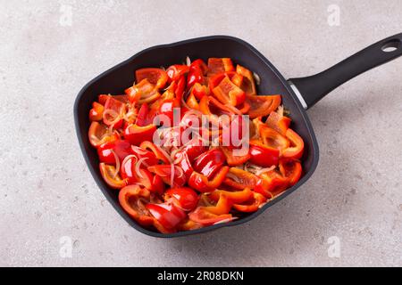 Bratpfanne mit geschmorter roter Paprika und Zwiebel auf beigefarbenem strukturiertem Hintergrund, Draufsicht. Stufe des Kochens köstliche rote Pfeffertorte oder andere Stockfoto