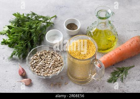 Zutaten für vegane Schnitzel: Hirse, Samen, Karotten, Kräuter, Knoblauch, Gewürze und Olivenöl auf grauem, strukturiertem Hintergrund Stockfoto