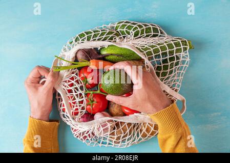 Man nimmt Pfirsichfrucht aus der Gitterpackung mit Obst und Gemüse. Umweltfreundliches Einkaufen Stockfoto
