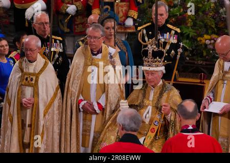 König Karl III. (Vorne in der Mitte) sitzt in St. Edwards Stuhl, auch bekannt als Krönungsstuhl, trägt St. Edward's Crown und hält während seiner Krönungszeremonie in Westminster Abbey, London, das Zepter des Sovereign mit der Taube (in der linken Hand) und das Zepter des Sovereign mit Kreuz (in der rechten Hand). Foto: Samstag, 6. Mai 2023. Stockfoto