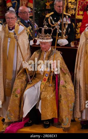 König Karl III. (Vorne in der Mitte) sitzt in St. Edwards Stuhl, auch bekannt als Krönungsstuhl, trägt St. Edward's Crown und hält während seiner Krönungszeremonie in Westminster Abbey, London, das Zepter des Sovereign mit der Taube (in der linken Hand) und das Zepter des Sovereign mit Kreuz (in der rechten Hand). Foto: Samstag, 6. Mai 2023. Stockfoto