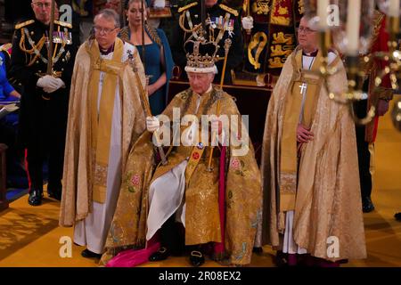 König Karl III. (Vorne in der Mitte) sitzt in St. Edwards Stuhl, auch bekannt als Krönungsstuhl, trägt St. Edward's Crown und hält während seiner Krönungszeremonie in Westminster Abbey, London, das Zepter des Sovereign mit der Taube (in der linken Hand) und das Zepter des Sovereign mit Kreuz (in der rechten Hand). Foto: Samstag, 6. Mai 2023. Stockfoto