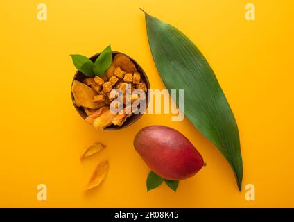 Von Mango getrocknete Scheiben und Kugeln in Schüssel auf gelbem Hintergrund. Draufsicht. Stockfoto