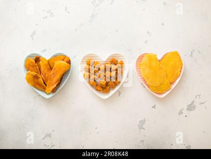 Getrocknete Mangoscheiben und -Kugeln in herzförmigen Platten auf hellem Hintergrund. Draufsicht. Stockfoto