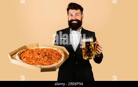 Restaurant oder Pizzeria. Lächelnder bärtiger Mann mit Pizza in der Schachtel und kaltem Bier. Fastfood. Italienisches Essen. Geschäftsmann im Anzug mit leckerer Pizza und einem Becher Stockfoto