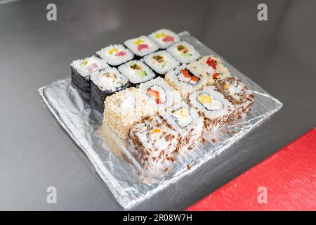 Ein Set mit verschiedenen Sushi auf einem Folienlaken auf dem Küchentisch. Hochwertiges Foto Stockfoto