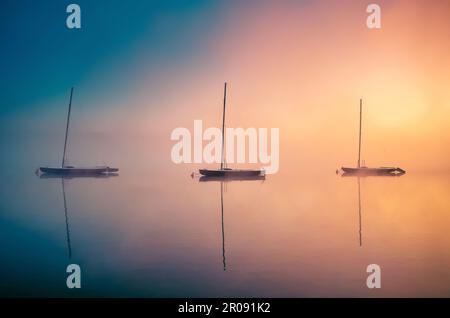 Farbenfroher nebiger Morgen auf dem See. Boote, die sich im Wasser am Parpocany-See in Tychy, Polen, spiegeln. Stockfoto