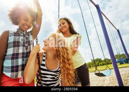 Die glücklichen Zeiten noch glücklicher zu machen. Junge Mädchen, die auf den Schaukeln im Park spielen. Stockfoto