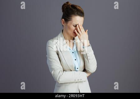Gestresste, stilvolle Mitarbeiterin in einem leichten Business-Anzug isoliert auf Grau. Stockfoto